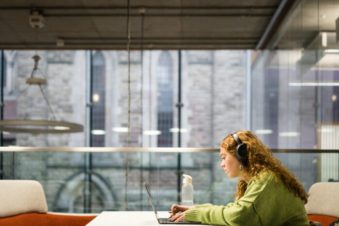Photograph of a student working at a laptop in the Library wearing earphones