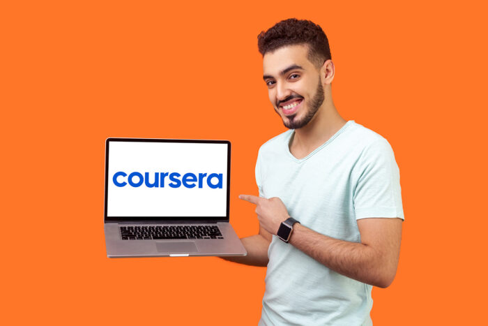 Promotional image for Coursera. Young Asian male holds a laptop which displays the Coursera logo.