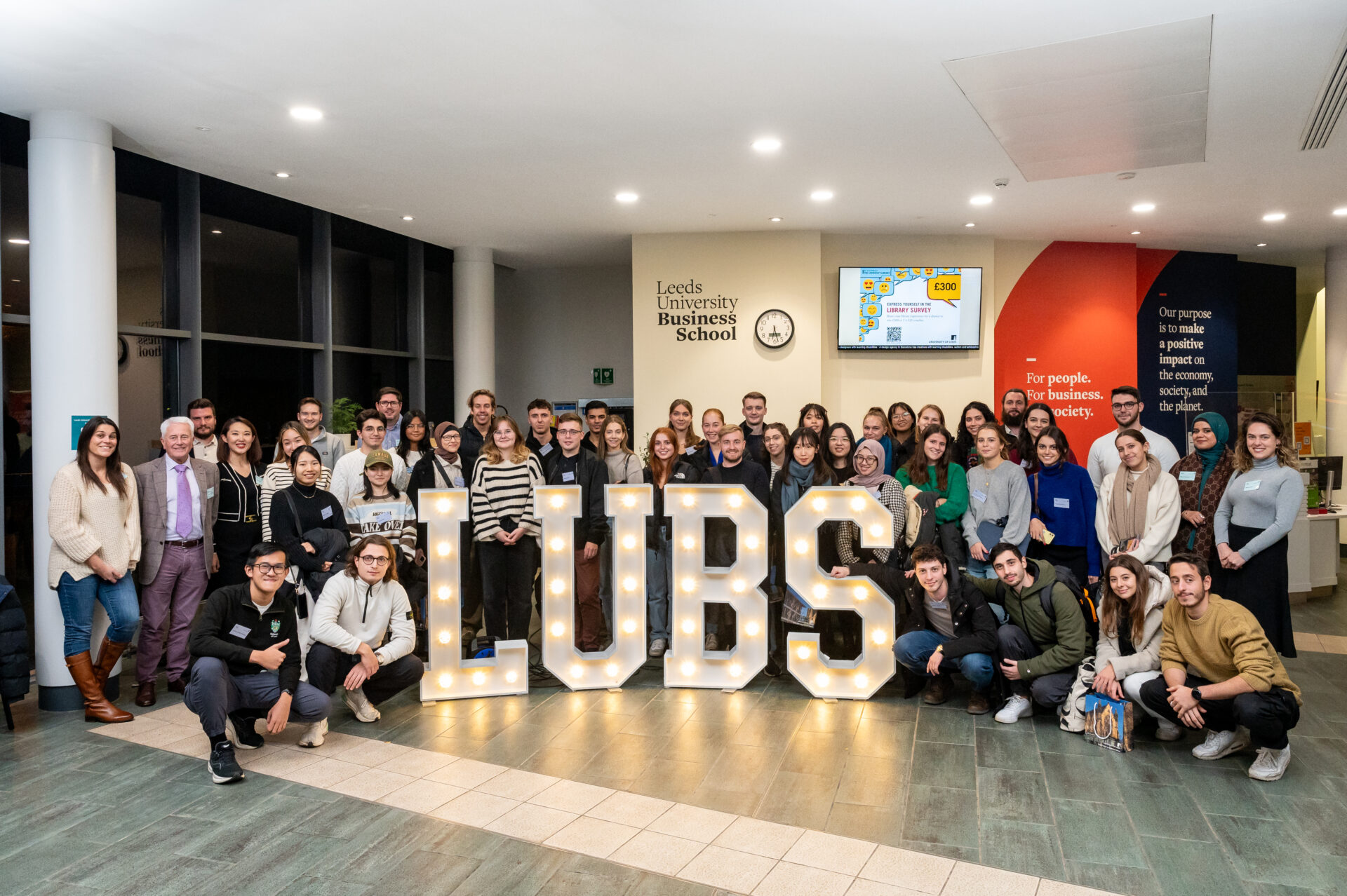 A large group of Study abroad students who have just arrived in Leeds are gathered, smiling and happy, around large lit-up letters spelling L U B S