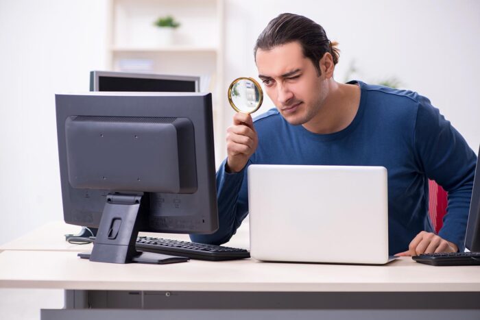 Man investigating computer with a magnifying glass, signifying troubleshooting an IT issue.